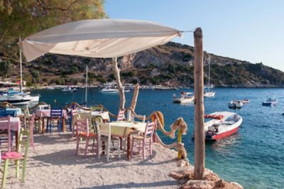 Café am Strand von Agios Nikolaos, mit bunten Holzstühlen unter einem Sonnensegel