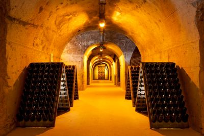 Galerie voûtée de la cave Taittinger, où une lumière orangée éclaire les bouteilles de champagne entreposées