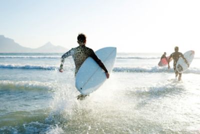 A trio of surfers running into the sea as the sun reflects off the water