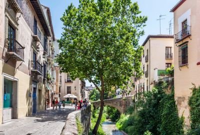 Calle en Granada con edificios antiguos, junto a un pequeño río y vegetación.