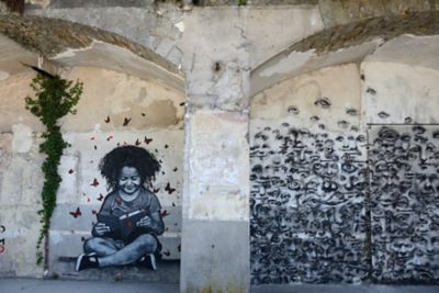 Black-and-white street murals, of a reading child and merging faces, in Paris
