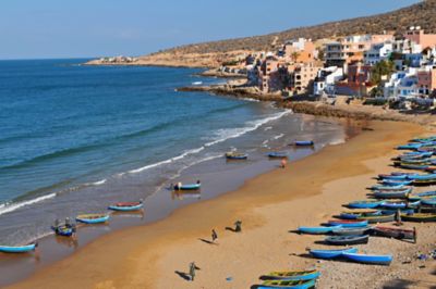 A beach in Taghazout, Morocco, with colourful fishing boats, golden sands and calm blue waters