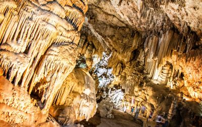 Interior de la cueva con formaciones rocosas iluminadas y turistas.