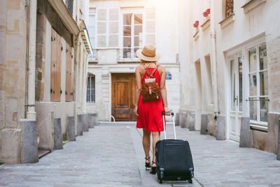 Une femme portant une robe rouge et un chapeau qui marche en tirant sa valise lors d’un voyage
