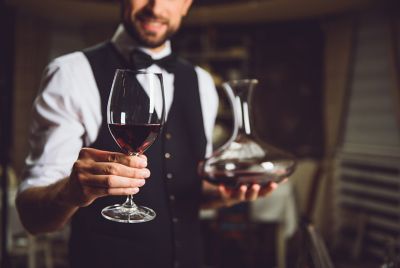 A server holding a carafe and a glass of red wine