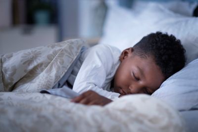 A young child in white pyjamas sleeping peacefully in a plush bed