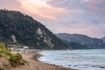 Tranquil Glyfada Beach in Corfu, Greece, with a sandy shore backed by pine-covered hills