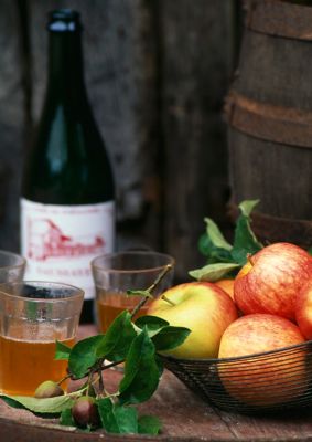 Verres de cidre sur une table rustique, avec pommes dans une corbeille et bouteille de cidre en arrière-plan
