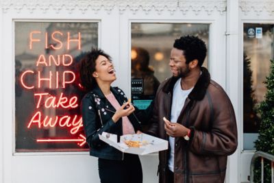 Couple having fun sharing fish and chips outside a takeaway store