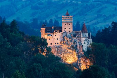 Gothic Bran Castle lit up in the evening standing in forested hills