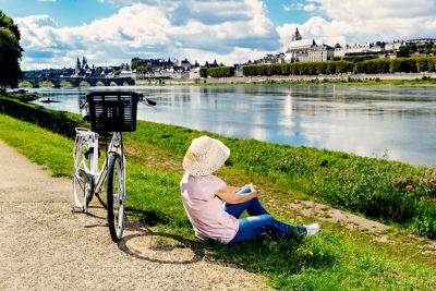 Une femme portant un chapeau, un t-shirt rose et un jeans fait une pause sur les bords de la Loire après une balade en vélo