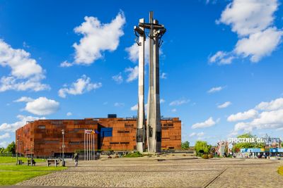 A tall steel monument and the ochre building of the European Solidarity Centre, Gdańsk
