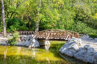 Puente de madera arqueado sobre un estanque verdoso rodeado de rocas blancas y densa vegetación