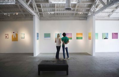 A pair of visitors discussing a row of abstract canvases in a spacious art gallery