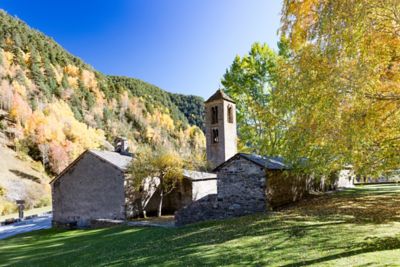 Iglesia medieval situada en un valle de montaña con árboles otoñales y cielo azul