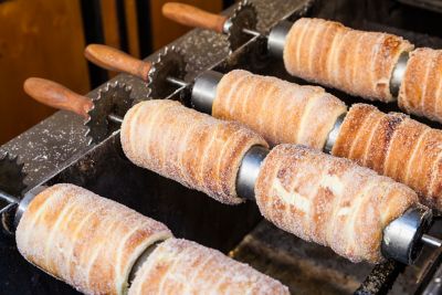 Cylindrical trdelník pastry, sugar-dusted and golden, on a grill in Prague