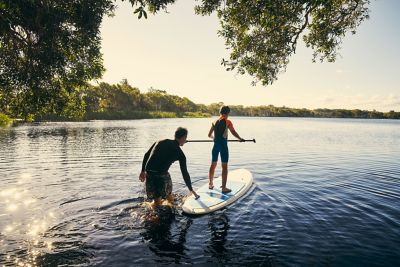 Un père apprend à son fils à faire du stand up paddle sur un étang