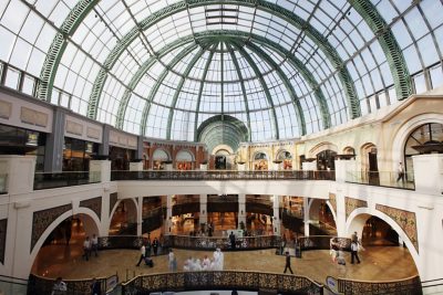 A bustling shopping mall with a stunning glass dome ceiling. Shoppers stroll along the mall's various levels, browsing the numerous high-end stores. The mall's elegant architecture, with its intricate details and warm lighting, creates a luxurious and inviting atmosphere.