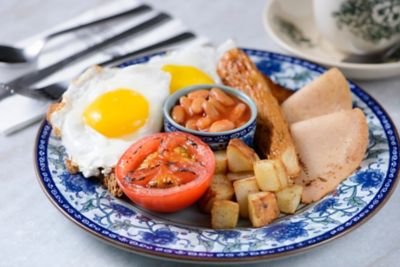 English Breakfast mit Bohnen, Tomate, Spiegelei und Schinken auf Teller mit blauem, floralem Design