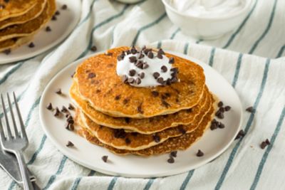 A stack of pancakes topped with chocolate chips and cream