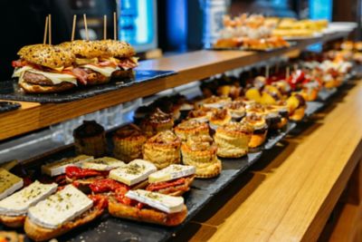 Mostrador de bar repleto de pintxos y tapas variadas, incluyendo mini hamburguesas