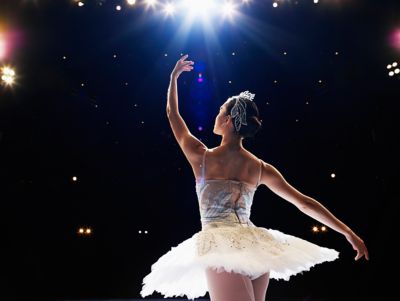A ballerina on a theatre stage, in a sequinned white outfit with arms in fourth position