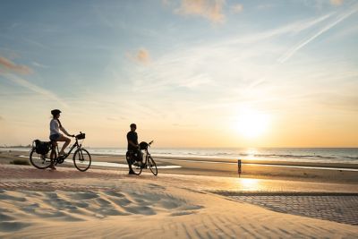 Un couple fait une balade à vélo sur la plage au coucher du soleil