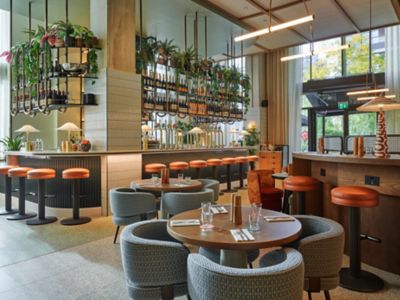 Tables et comptoir dans le bar du TRIBE London Canary Wharf, avec plantes suspendues