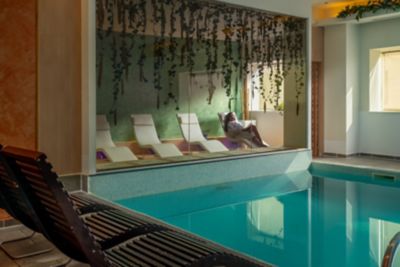 Piscina interior de hotel con tumbonas de madera en primer plano y zona de relax tras un cristal
