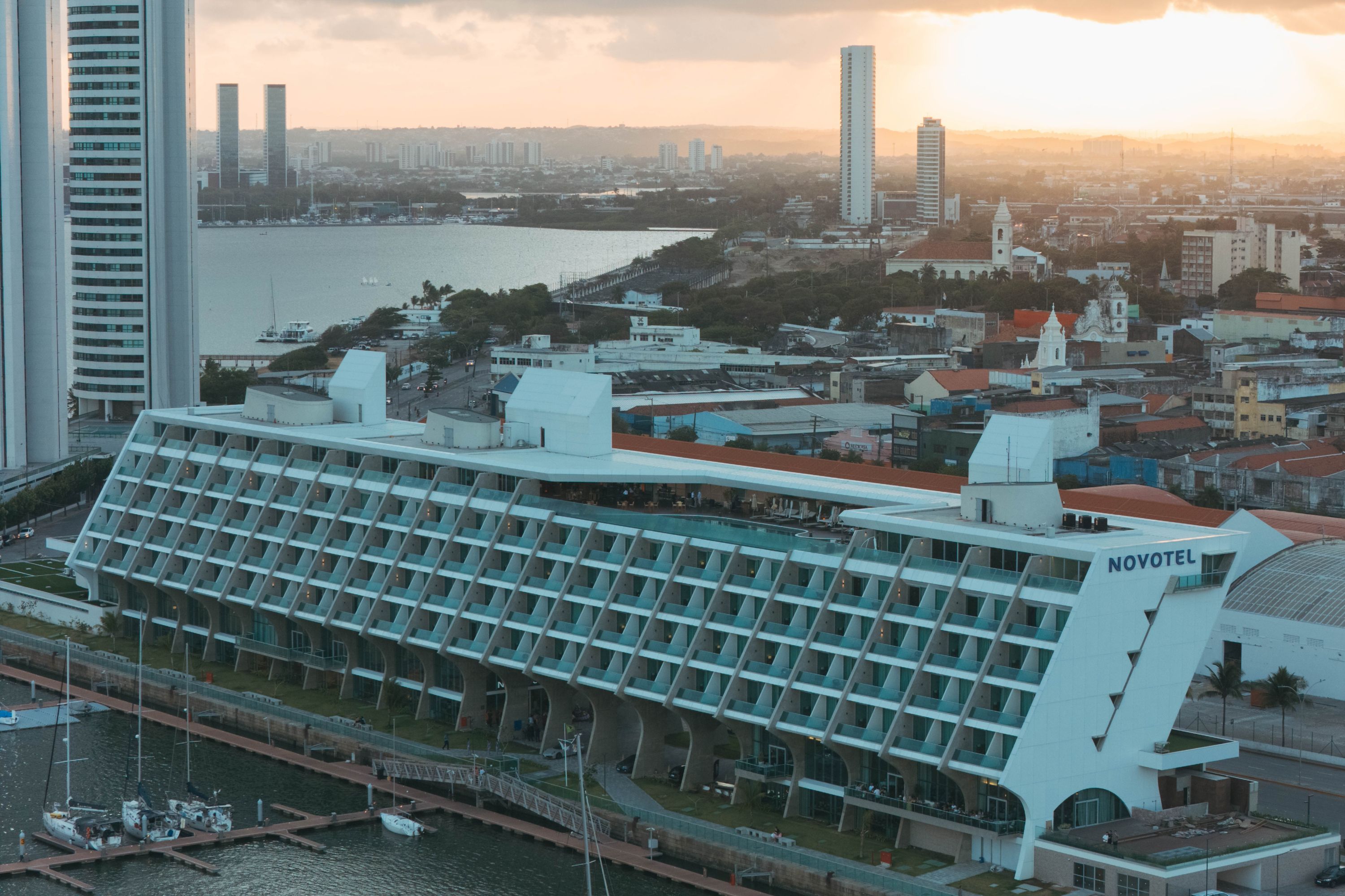 Sunset over a cityscape featuring a modern Novotel hotel