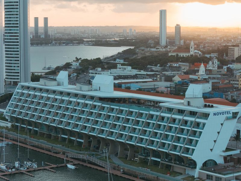 Sunset over a cityscape featuring a modern Novotel hotel
