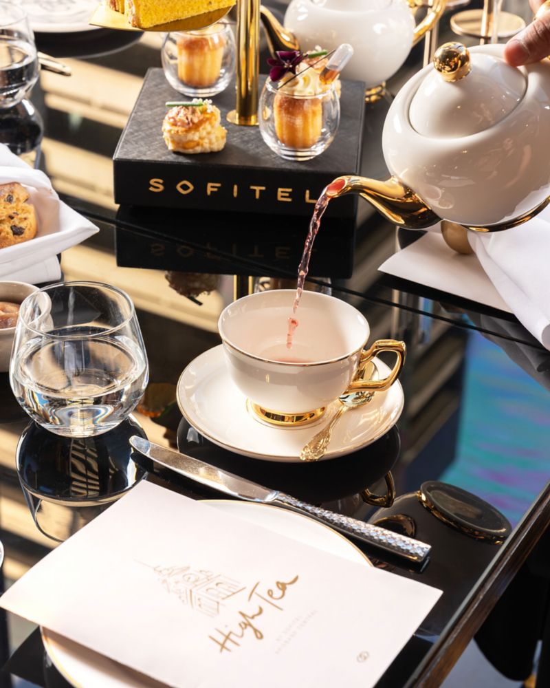 Tea being poured into teacup on a table set for high tea and a menu on the table