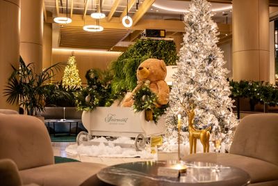 A giant teddy bear in a sled, next to a Christmas tree