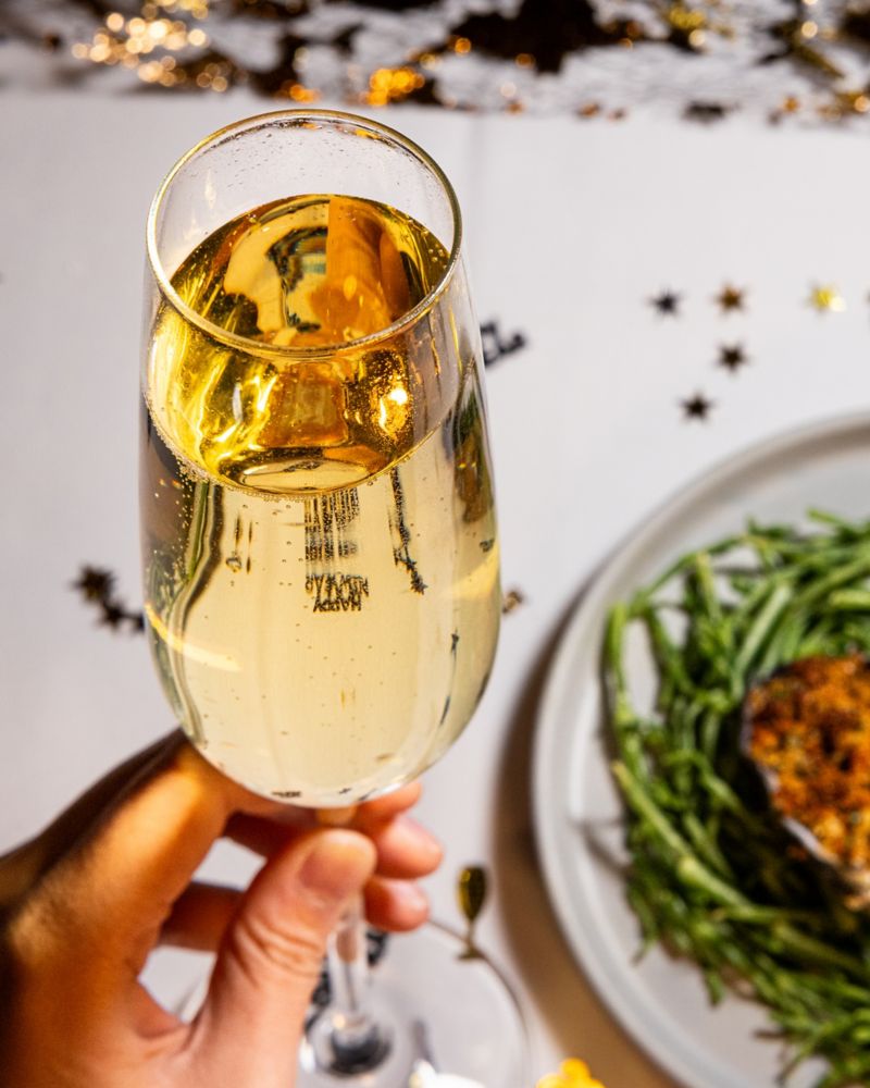 A hand holding a glass of champagne over a plate of food