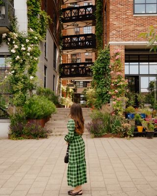 Une femme en robe verte qui se tient devant d’authentiques bâtiments en briques, ornés de plantes et de fleurs, dans le centre de Rotterdam