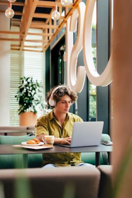Un digital nomad travaille sur son ordinateur portable en écoutant de la musique pour se concentrer, dans la salle de petit déjeuner d'un hôtel Novotel
