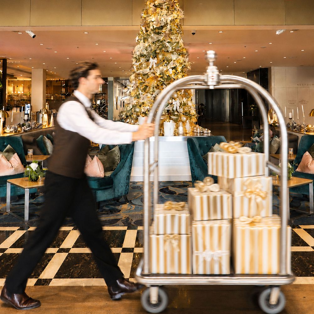 Staff member pushing lugagge trolly with christmas presents across lobby in front of christmas tree