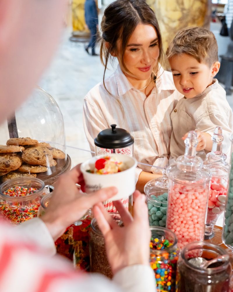 Man offering ice cream from an ice cream cart that says scoops sweets & soda