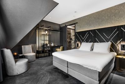 Chambre au design élégant, équipée d’un lit double et de deux fauteuils et décorée dans des tons noir et blanc, à l’hôtel Le Marin Hotel Rotterdam City