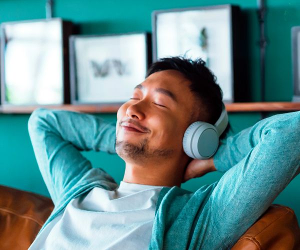 A smiling person with a large afro hairstyle, wearing a denim jacket and yellow headphones around their neck, sits on steps. To the left, there is an Ibis logo on a gradient background with red and green hues. Perfect for leisure or business stays, enjoy 15% OFF your next visit!