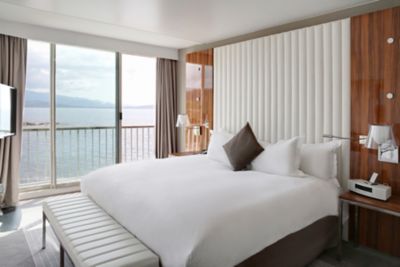 A calm hotel room with high-end bedding and large balcony doors with ocean views