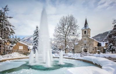 Fuente helada e iglesia de piedra en un pueblo nevado de montaña