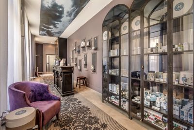 Entrée du spa de La Cour des Consuls Hotel & Spa Toulouse - MGallery Collection comprenant un fauteuil violet et des étagères vitrées présentant des produits cosmétiques
