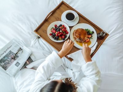 a girl in bed eating pancakes, berries, and coffee off a wooden try
