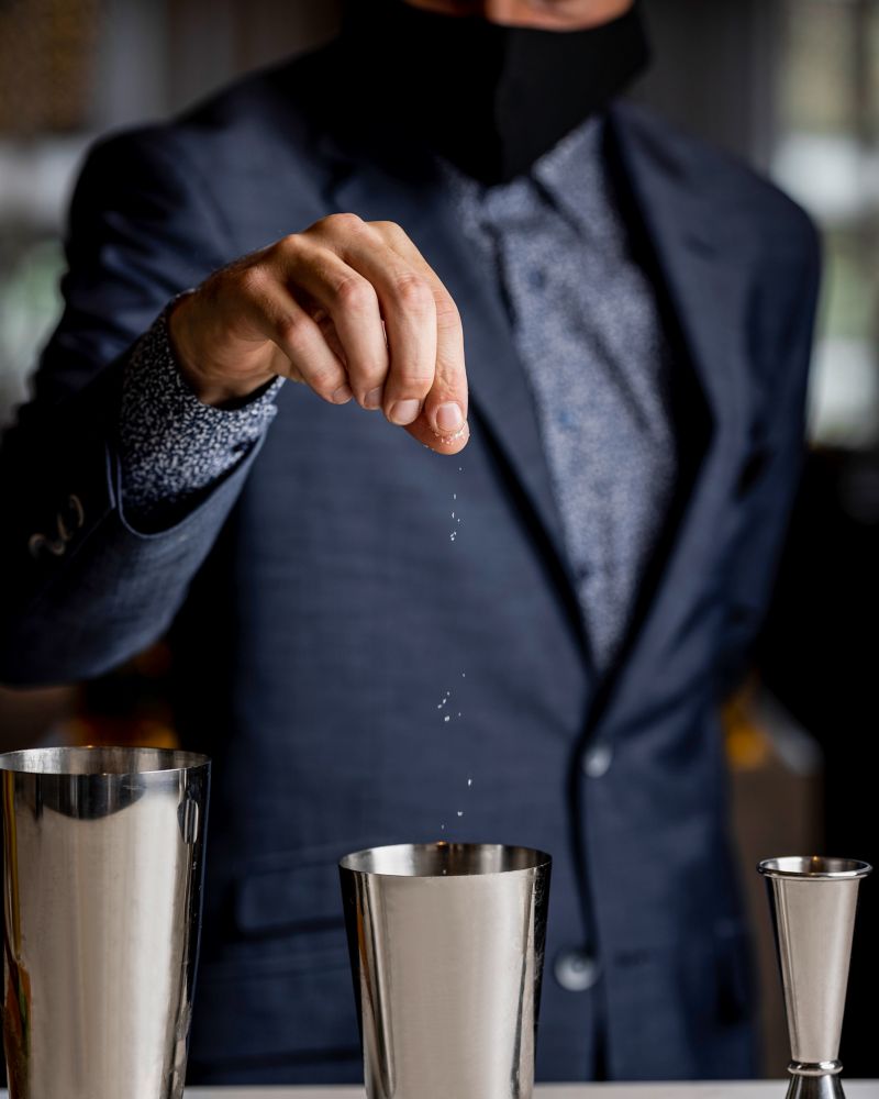 A bartender sprinkling something into a mixing tin