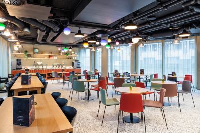 Restaurantbereich im ibis Styles Bern City mit bunten Stühlen und Industrie-Elementen an der Decke