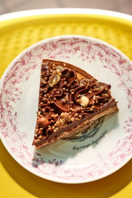 Üppiges Tortenstück mit Schokoladenguss und Nüssen auf rosa verziertem Teller