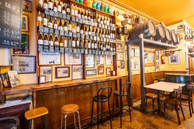 Interior de bar bodega tradicional con botellas, barriles, taburetes de barra y mesas