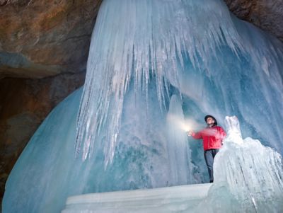 Mann mit roter Jacke und Taschenlampe unter gefrorenem Wasserfall in der Eisriesenwelt Werfen