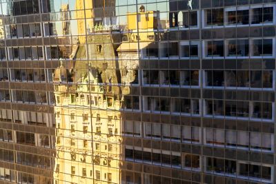 Reflection of a historic building with a green roof and ornate details in the glass windows of a modern office tower.